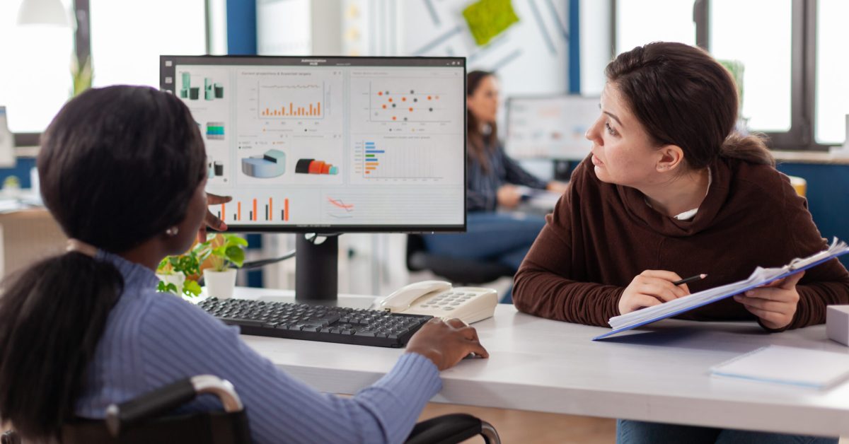 Manager discussing with invalid african woman company development plan Businesswoman discussing with invalid disabled paralysed african woman company development plan. Handicapped black leader explainig project strategy to manager corporate in strat up business office.