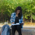 A young woman studying with books outdoors in a lush Delhi park, showcasing focus and tranquility.